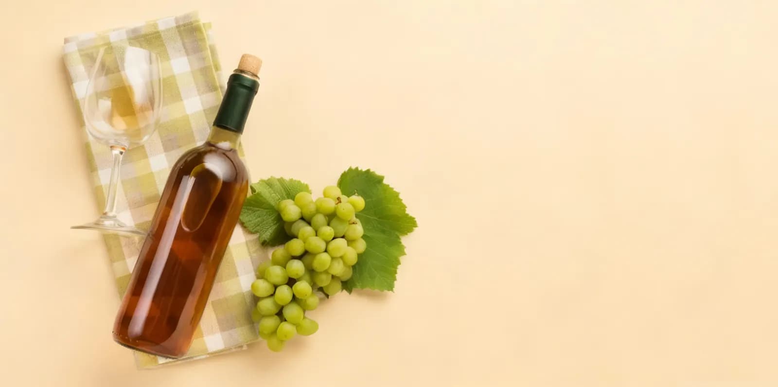 Botella de vino blanco con un racimo de uvas sobre un mantel de cuadros